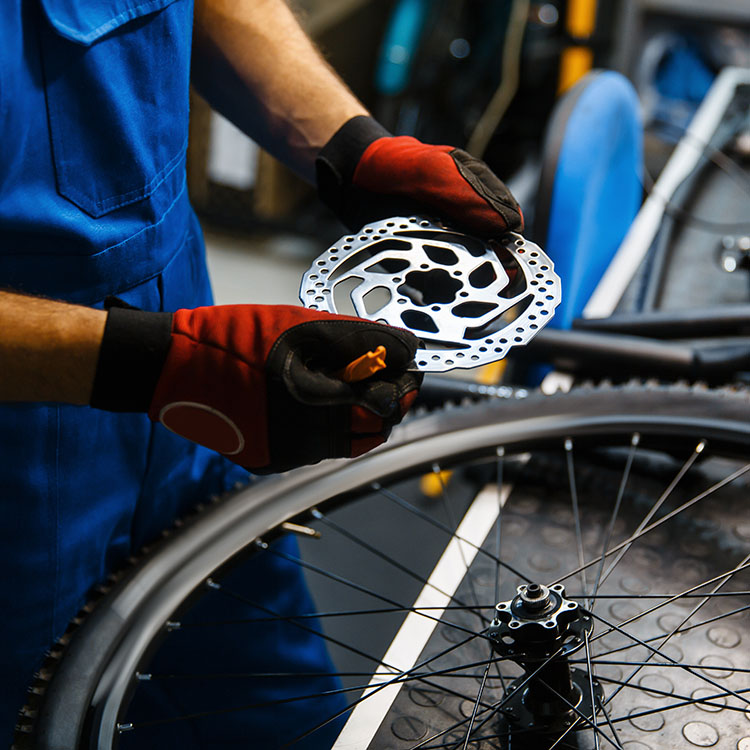 Fahrradmechaniker mit Handschuhen montiert Bremsscheibe an einem Vorderrad in der Werkstatt – professioneller Service bei Diermann - Bergsieger GmbH