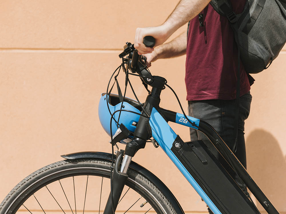 E-Bike-Leasing für Beruf und Alltag – Diermann - Bergsieger GmbH Mann mit Rucksack und Helm steht mit E-Bike vor orangefarbener Wand – moderne Mobilität durch Fahrrad-Leasing bei Diermann - Bergsieger GmbH